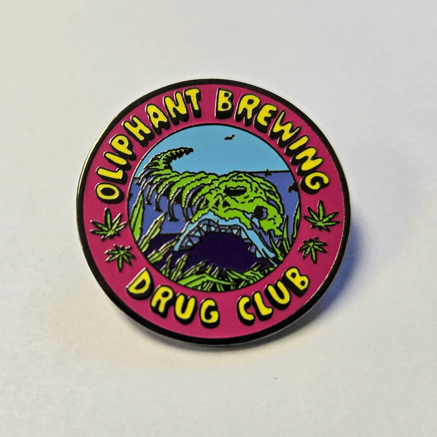 Oliphant Brewing Drug Club enamel pin with dinosaur skull and cannabis leaves on pink border