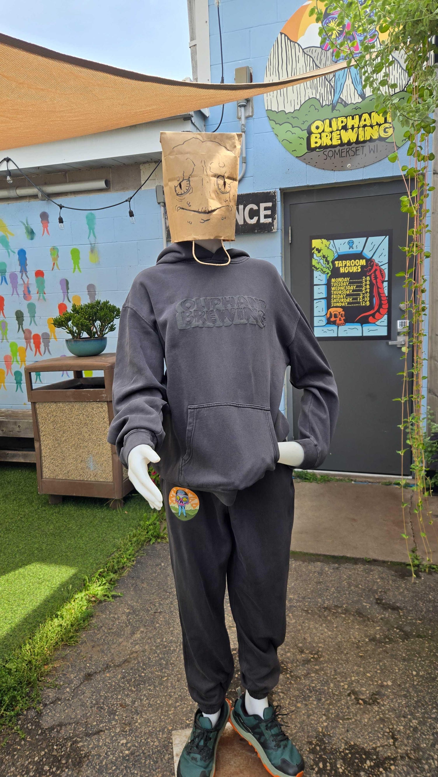Mannequin in Oliphant Brewing hoodie, paper bag mask, outside brewery entrance with mural
