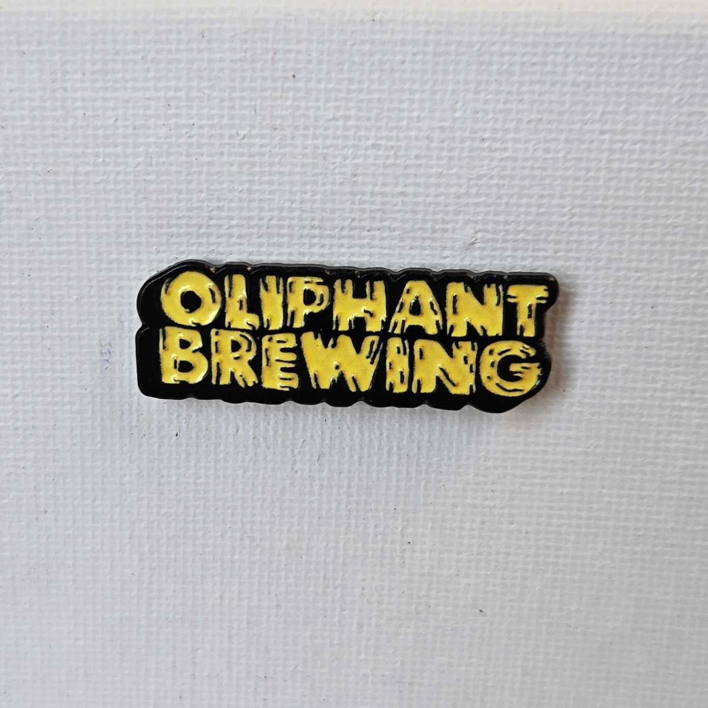 Oliphant Brewing yellow enamel pin on white textured background