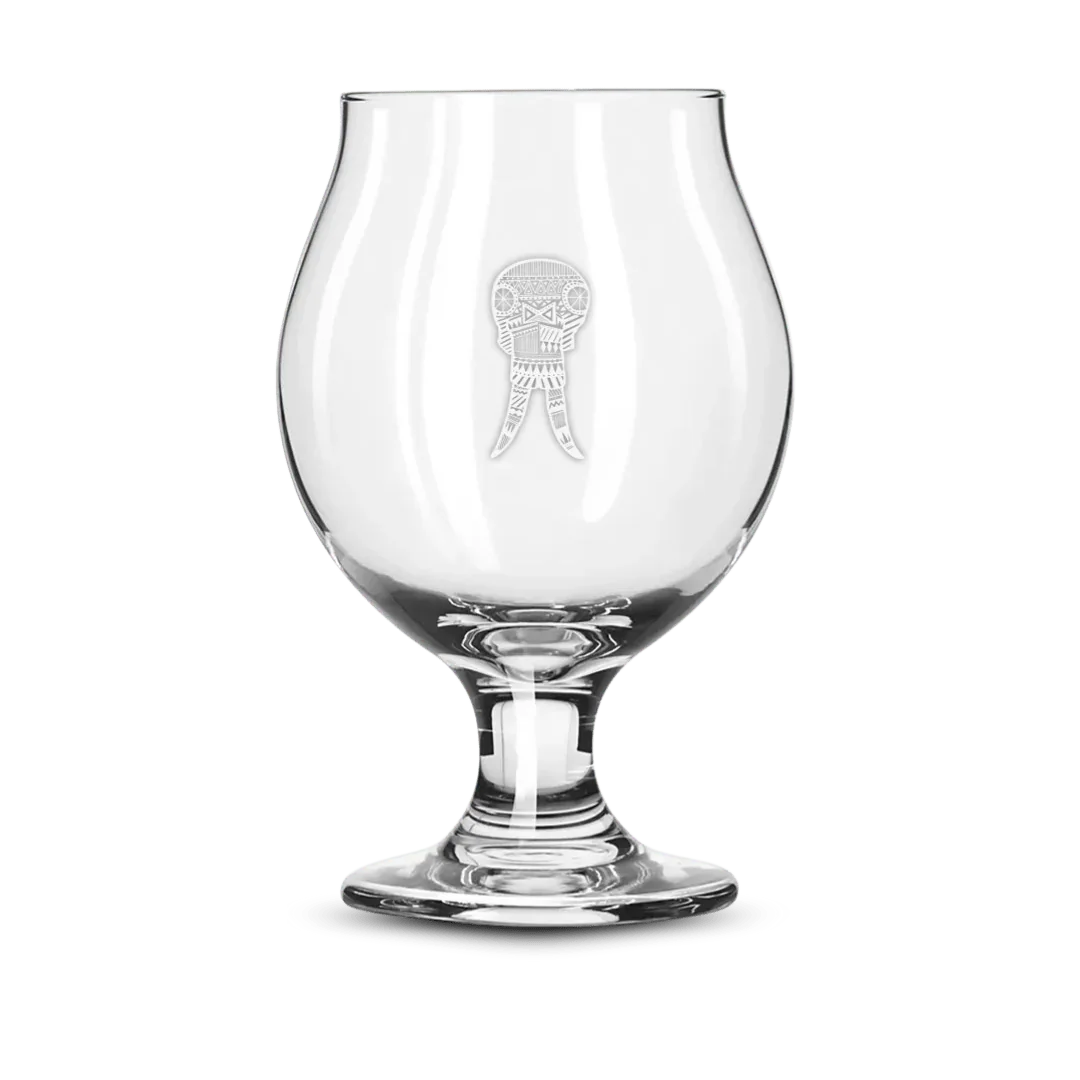 Clear snifter beer glass with etched geometric skull design on a green background