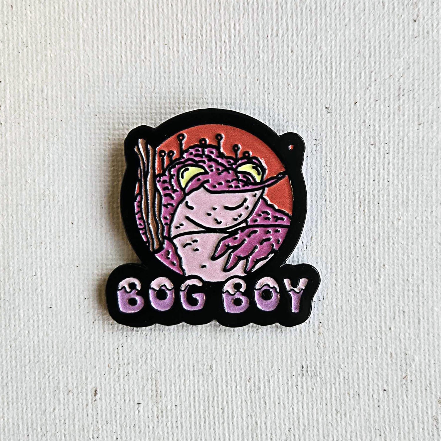 Bog Boy enamel pin with pink frog cartoon and purple lettering on canvas background