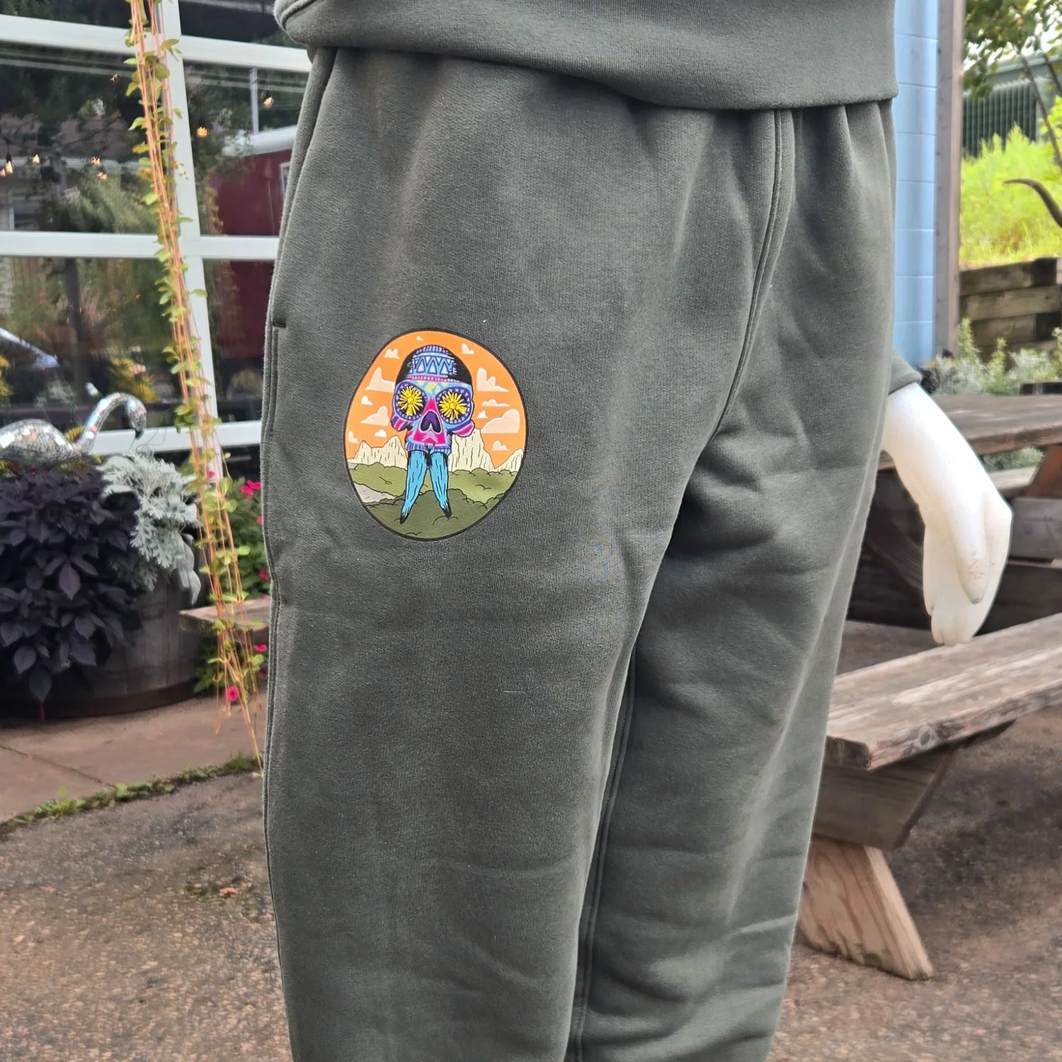 Olive green sweatpants with colorful skull patch on mannequin outdoors