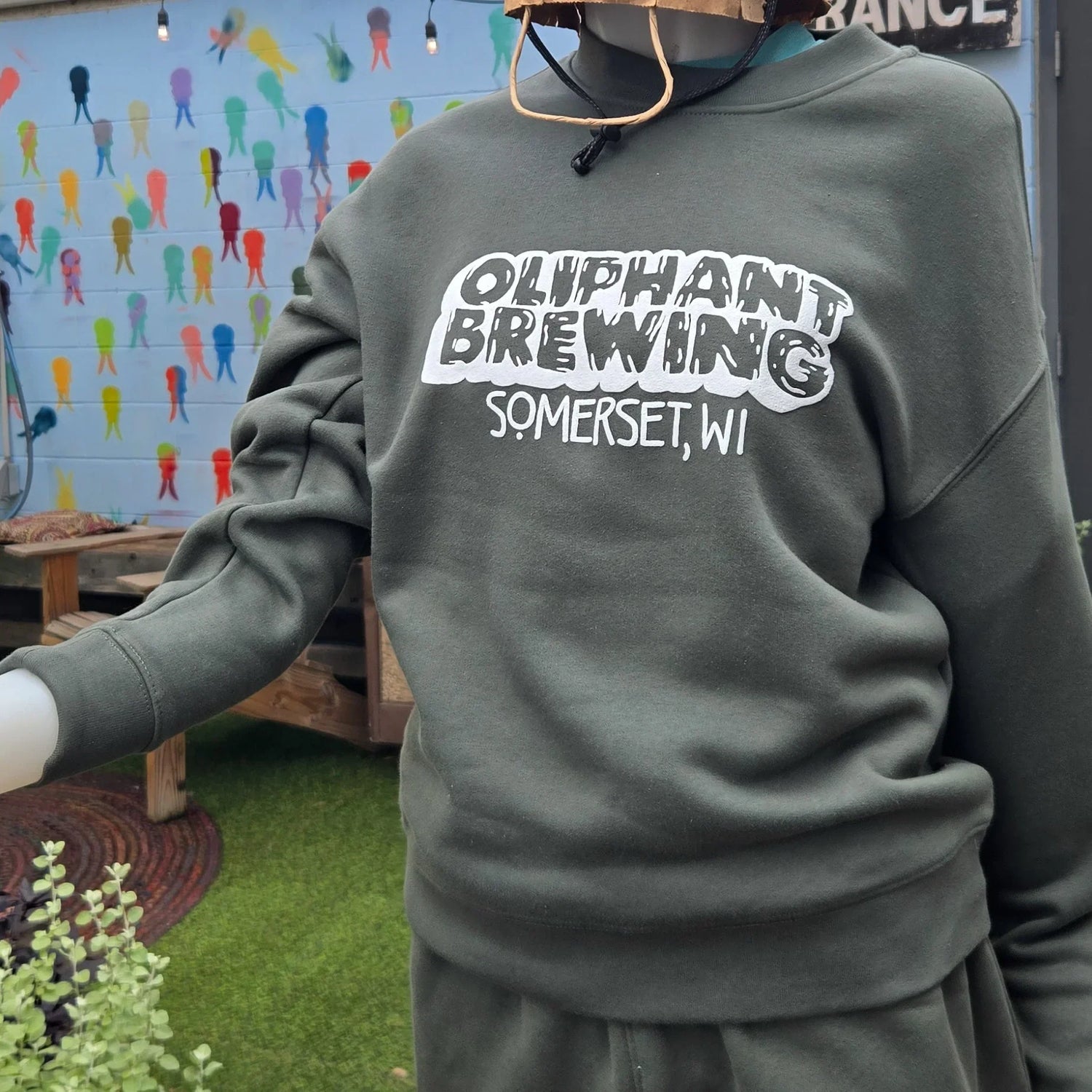 Oliphant Brewing Somerset WI green sweatshirt on mannequin, outdoor colorful mural background
