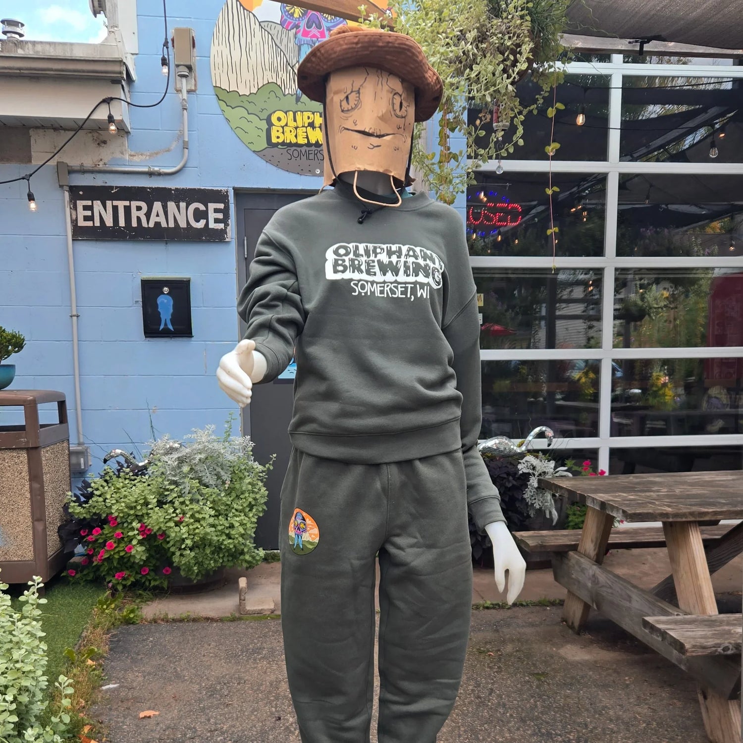Mannequin in Oliphant Brewing sweatsuit outside brewery entrance, wearing paper bag mask and hat