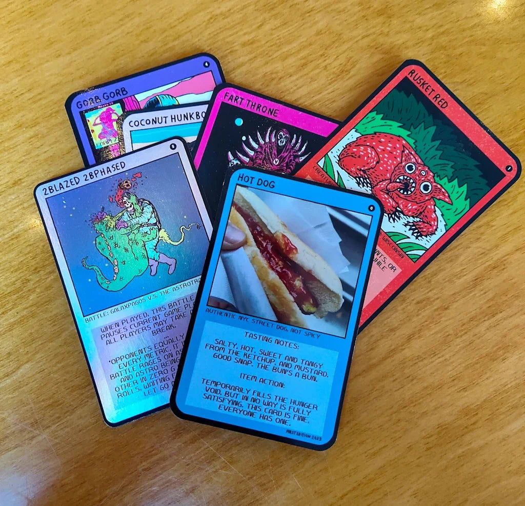 Colorful trading cards featuring unique illustrations and a hot dog photo on wooden table.