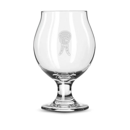 Clear snifter beer glass with etched geometric skull design on a green background